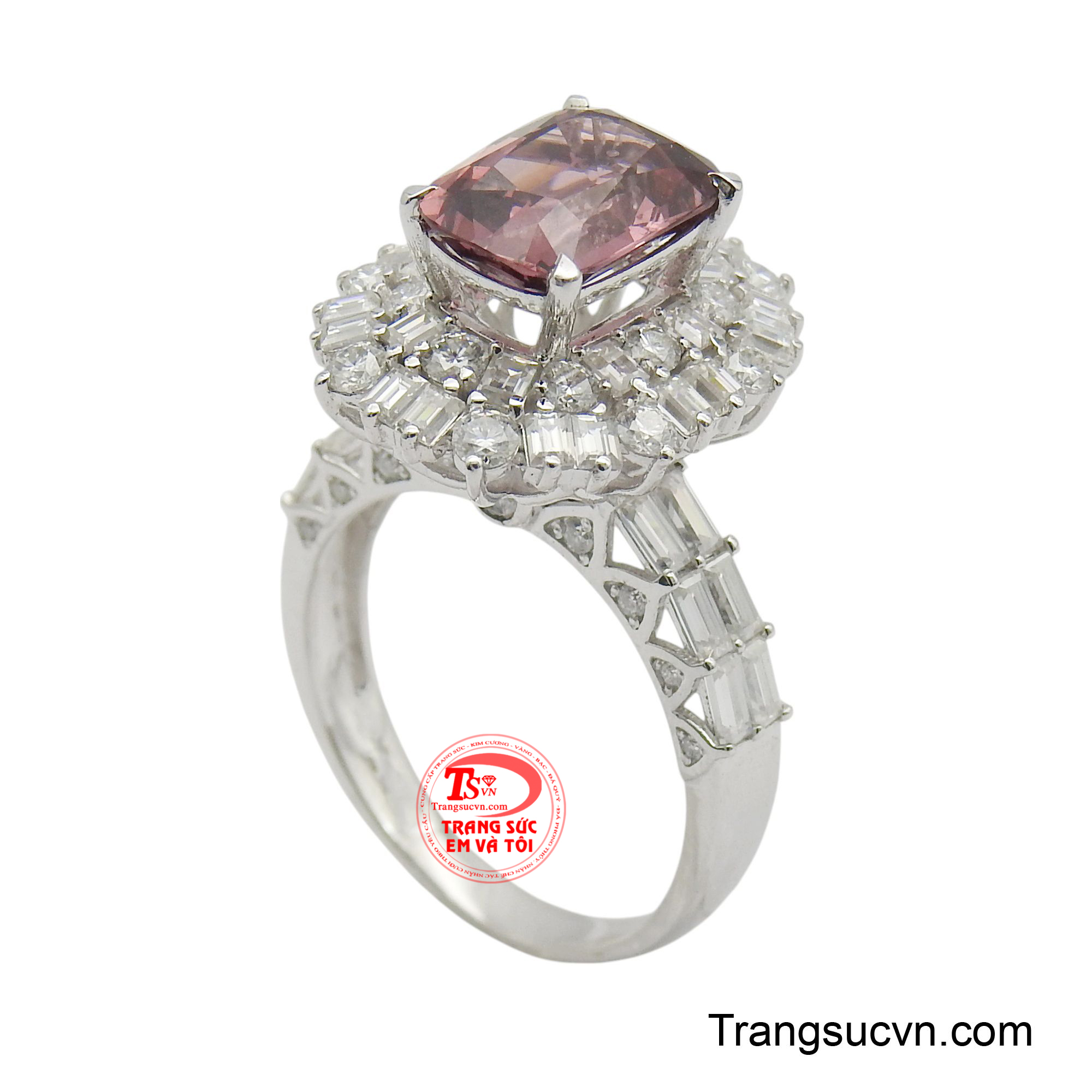 Tâm điểm của thiết kế là viên đá chủ hình chữ nhật lớn, mang sắc hồng đào tinh tế, được bao quanh bởi một vòng hào quang rực rỡ của vô số viên đá nhỏ lấp lánh, tạo hiệu ứng phản chiếu ánh sáng tuyệt đẹp.