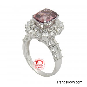 Tâm điểm của thiết kế là viên đá chủ hình chữ nhật lớn, mang sắc hồng đào tinh tế, được bao quanh bởi một vòng hào quang rực rỡ của vô số viên đá nhỏ lấp lánh, tạo hiệu ứng phản chiếu ánh sáng tuyệt đẹp.