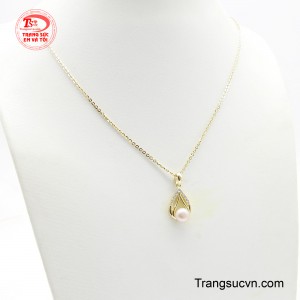 Mặt dây chuyền được thiết kế tinh xảo, với viên ngọc trai ánh hồng đào lấp lánh nằm giữa khung vàng uốn lượn được điểm xuyết những viên đá nhỏ.