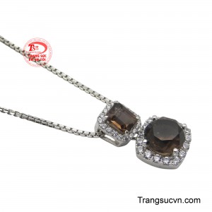 Phía dưới, viên thạch anh khói lớn hình tròn được ôm trọn bởi những viên kim cương lấp lánh, tạo nên một điểm nhấn lộng lẫy và quyến rũ, biểu trưng cho sự viên mãn và tỏa sáng.