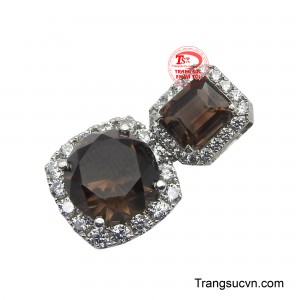 Phía dưới, viên đá lớn hình tròn được bao quanh bởi một vòng kim cương lấp lánh, tạo nên hiệu ứng rực rỡ và quyến rũ, tôn vinh nét duyên dáng của người phụ nữ.