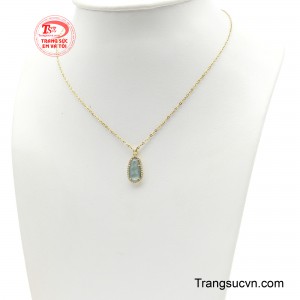Điểm nhấn của bộ trang sức là viên ngọc xanh dáng hạt đậu, sở hữu sắc màu trầm nhẹ, mềm mại cùng những đường vân tự nhiên như được lưu giữ từ lòng đất qua tháng năm. 